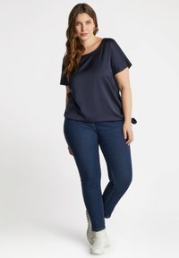 Top de seda azul marino con un corte holgado y mangas cortas, combinado con jeans ajustados azul oscuro y zapatillas blancas. Textura suave, diseño sencillo.