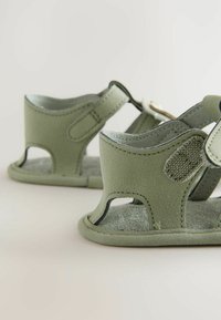 Gröna, mjuka mockasandaler med urtag på sidorna, justerbar rem och texturerad innersula. Robust design med synliga sömsmycken.