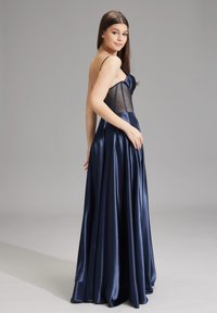 Abito da sera in satin navy con corpetto aderente, pannelli trasparenti e una gonna fluente che scende elegantemente fino al pavimento. Spalline sottili regolabili.