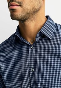 Granatowa i jasnoniebieska koszula w kratę z kołnierzem zapinanym na guziki i pojedynczym guzikiem przy szyi, wykonana z tkaniny o miękkiej fakturze.