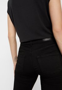 Jeans pretos de cintura alta com um corte justo, apresentando bolsos traseiros e detalhes de costura subtis. Textura suave e design limpo.