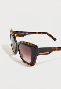 Nadrozměrné sluneční brýle s želvovinovým vzorem a gradientními čočkami. Mají elegantní hranaté obroučky a logo "KARL LAGERFELD" na stranici.