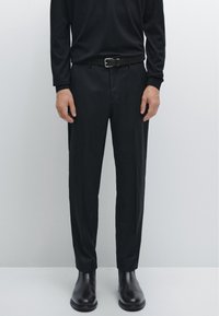 Czarne, dopasowane spodnie garniturowe o smukłym kroju, z gładką fakturą i przednimi kieszeniami, zestawione z czarnymi skórzanymi botkami za kostkę i paskiem.