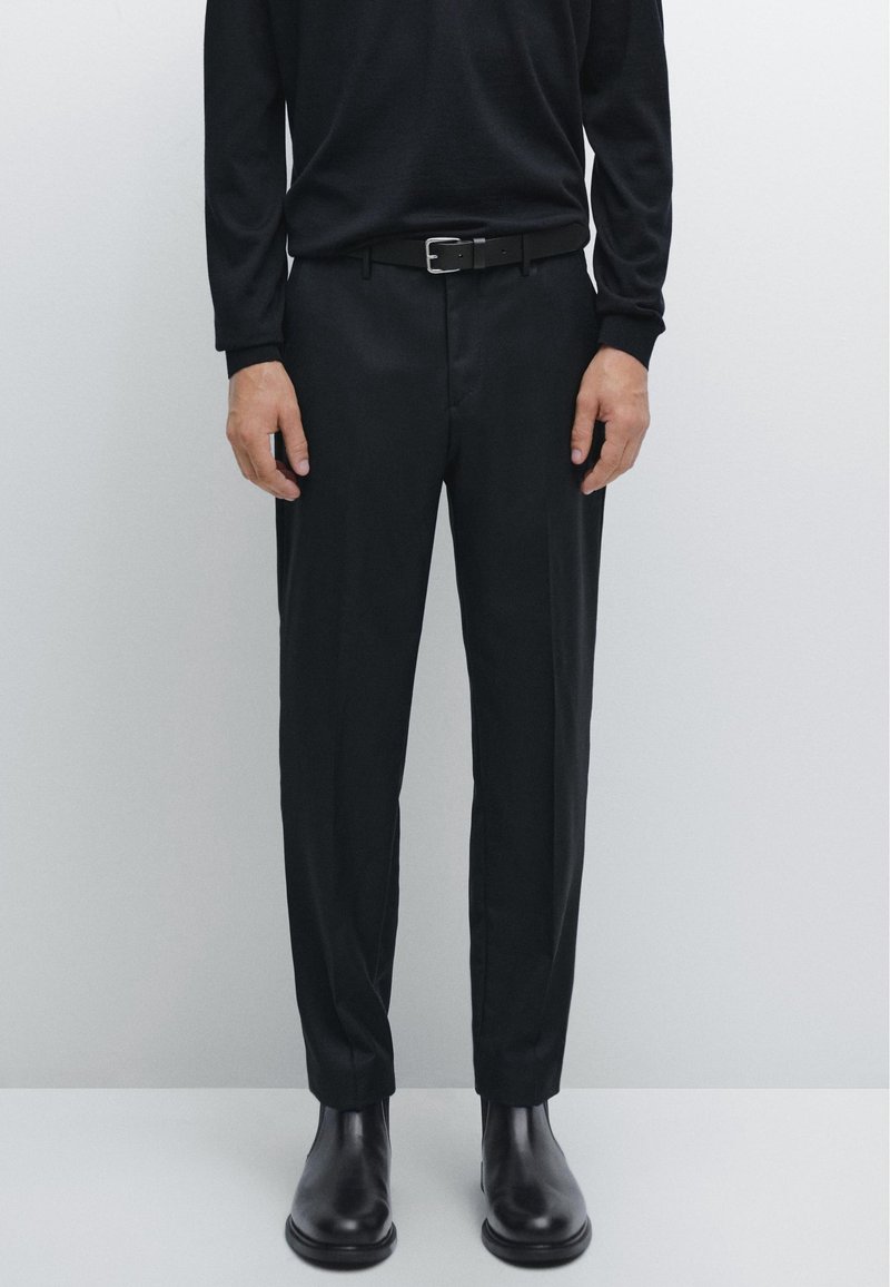 Czarne, dopasowane spodnie garniturowe o smukłym kroju, z gładką fakturą i przednimi kieszeniami, zestawione z czarnymi skórzanymi botkami za kostkę i paskiem.