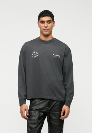 Tumehall pikkade varrukatega t-särk ümmarguse kaelusega. Ees on valge tekst ja ümmargune graafika. Kombineeritud mustade nahkpükstega.