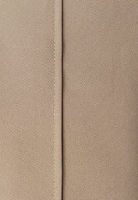 Tessuto beige con una superficie liscia, caratterizzato da una cucitura centrale delineata da cuciture a contrasto. Vista ravvicinata della superficie del materiale.