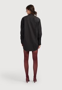 Čierne šaty s vertikálnymi pruhmi a dlhými rukávmi, zakriveným spodným okrajom a jednofarebným zázemím; nosené s vínovými pančuchami a zodpovedajúcimi lodičkami.