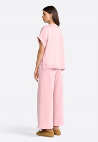 Completo in cotone rosa misto, composto da una maglietta a maniche corte con spacchi laterali e pantaloni a gamba larga, abbinato a scarpe slip-on beige.