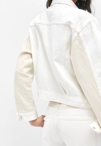 Biała denimowa kurtka z kontrastującymi beżowymi rękawami, krótki fason i zapięcie na guziki przy mankietach. Posiada metkę z tyłu oraz gładką teksturę.
