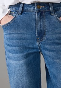 Blue denim jeans with a slightly faded finish, featuring three pockets, a button closure, and contrasting stitching along the seams.
