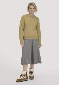Senfgelber gestrickter Pullover mit geripptem Saum, grauer Midirock und braunen, mit weißem Akzent und Schnürsenkeln versehenen, mit Pelz gefütterten Stiefeln.