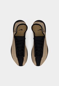 Ζευγάρι μπεζ και μαύρα αθλητικά παπούτσια Nike, εμφανιζόμενα από πάνω, με διατρητό σχέδιο και ορατό λογότυπο Nike στις εσώσες.