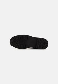 Suela de zapato de goma negra con surcos y relieves profundos, que presenta patrones circulares dispuestos de manera uniforme. Textura suave con una construcción sólida.