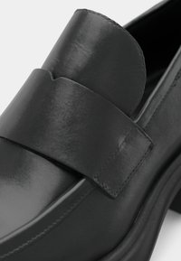 Black leather loafer featuring a wide strap and a smooth finish. The sole is thick and slightly rounded, emphasizing its contemporary design.
