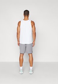 Top desportivo branco e calções cinzentos numa modelo, com um corte solto, tecido leve e design sem detalhes.