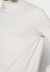 Hellbeige Rollkragenpullover in einem gerippten Strickmuster, mit hohem Kragen und schmalen Ärmeln, versehen mit sichtbaren Nähten.