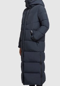 Lång mörkblå pufferjacka med huva, med en quiltad design, dragkedjefickor och justerbara snoddar. Slät, matt yta.