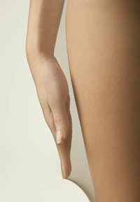 Nøgne, gennemsigtige strømpebukser hænger over en hånd og fremhæver en glat, transparent tekstur og subtil glans. Materialet er let og tætsiddende.