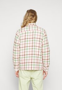 Plaid jacket featuring pink, green, and brown colors with a button-up design, long sleeves, and cuffed wrist details. Cotton material.