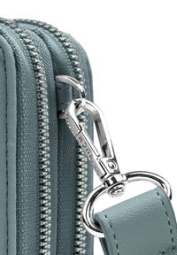 Tyrkysová kožená kabelka se stříbrným zipem a karabinou. Má textured povrch a hladce zakulacený úchyt na popruh.