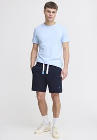 Svijetloplava majica s kratkim rukavima uparena s tamnoplavim hlačicama koje imaju bijelu vezicu. Bijeli sneakers s perforacijama upotpunjuju odjevnu kombinaciju.