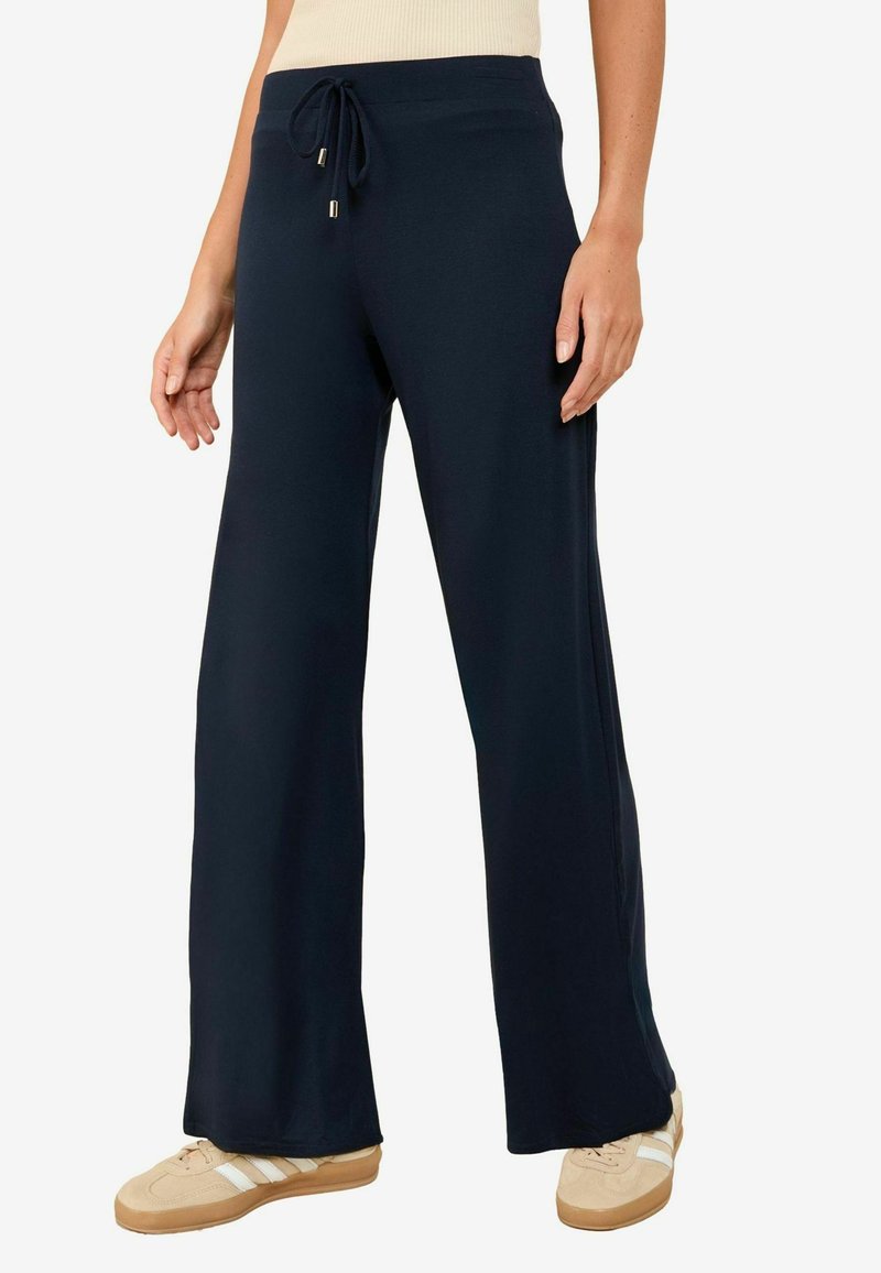 Pantalons larges bleu marine avec une taille à cordon, texture douce et fentes latérales, associés à des baskets crème avec trois bandes.