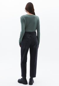 Camisa de manga larga verde combinada con jeans negros de cintura alta. Los jeans tienen un corte recto, bolsillos clásicos y se llevan con botas negras.