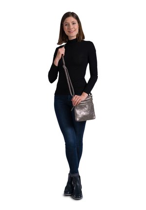 Metallic silver crossbody bag with a smooth texture, adjustable strap, and front zip pocket. Worn with fitted black top and dark jeans.