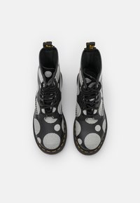 Stivali neri con un motivo a pois di diverse dimensioni. Realizzati in materiale resistente, presentano una punta tondeggiante, un design con lacci e dettagli di cucitura gialla.