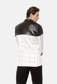 Czarna, sztuczna skóra na ramionach i kołnierzu, biała część z małymi czarnymi logo, dopasowany krój, długie rękawy oraz prosty tył z wentylacją.