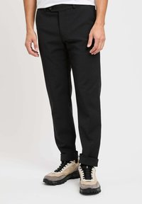 Pantaloni neri con design a gamba dritta, realizzati in tessuto testurizzato, con vita slim e orli arrotolati, abbinati a sneakers beige.