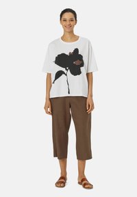 Witte t-shirt met korte mouwen met een groot zwart bloemmotief, gecombineerd met korte bruine broeken en bruine sandalen. Eenvoudige en casual outfit.