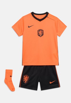 Oranžový futbalový dres s krátkym rukávom a čiernym golierom, čierne šortky a oranžové ponožky v rovnakej farbe, s erbom leva a logami Nike.