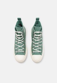 Wysokie trampki w miętowym kanwie z białymi sznurówkami, gumowymi podeszwami i strukturalnym wykończeniem, z pętelką z tyłu dla łatwego zakładania.
