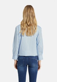 Ljusblå randig blus med puffärmar, tillverkad av ett mjukt tyg. Matchas med mörkblå jeans med bakfickor.