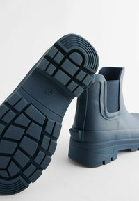 Sötétkék gumibakancs ankle stílusban, texturált talppal, elasztikus oldalsó panelekkel, sima felsőrésszel, kerek orral és sarokkal.