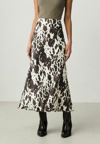 Jupe maxi en tissu crème avec un motif tacheté noir. Présente une texture lisse et un ourlet évasé, associée à des bottines noires.