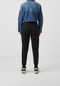 Džínová zkrácená bunda s knoflíkovými manžetami, zkombinovaná s černými přiléhavými tepláky a sportovní obuví s kombinací černých a stříbrných detailů.