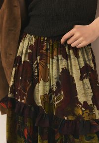 Fustă florală cu un amestec de culori cărămizii, verzi și crem, cu tiv ondulat și talie elastică. Material din amestec de bumbac cu textură.