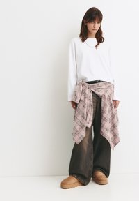 Weißes Langarmhemd, übergroßes karriertes Flanellhemd um die Taille gebunden, dunkle weite Jeans und beige Plateauschuhe.