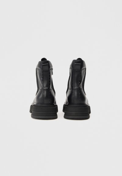 Schwarze Leder-Ankle-Boots mit einer strukturierten Oberseite, seitlichem Reißverschluss und einer dicken Gummisohle. Mit Zickzacknähten an den Seiten.