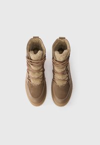 Barna vízálló csizmák puha gyapjúbéléssel, texturált gumitalppal és fűzőkkel. Felső része sima és bőrből készült.