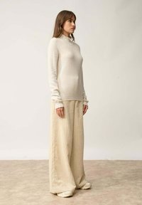 Beige gestrickter Rollkragenpullover kombiniert mit weiten, gerippten, cremefarbenen Hosen. Der Stoff ist weich und hat einen lockeren Sitz.