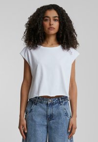 Fehér, rövidített póló kerek nyakkivágással és egyenes ujjakkal, párosítva magas derekú, fakó kék farmernadrággal, amelynek varrásai jól láthatóak.