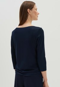 Navy blauwe lange mouwen top met een bateau halslijn, zachte stof, aansluitend ontwerp en een gedrapeerde achterkant. Soepele textuur met een elegante uitstraling.