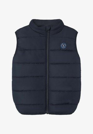 Gilet matelassé bleu marine avec un col haut, fermeture éclair et empiècements cousus horizontalement ; il présente un logo circulaire sur la zone de la poitrine.
