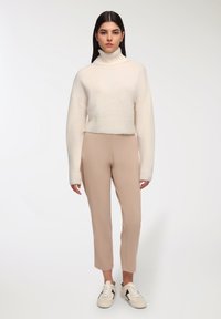 Biały pluszowy sweter z golfem, beżowe dopasowane spodnie i białe sneakersy z czarnymi akcentami. Miękka textura, skrócony fason z szerokimi rękawami.