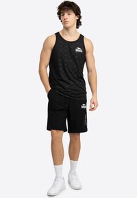 Sort tanktop med et subtilt mønster, parret med sorte shorts med en lynlås lomme. Hvide sneakers og ankelsokker fuldender outfittet.