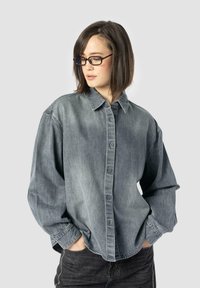 Denim shirt in faded gray, oversized fit with a button-down front, pointed collar, and long sleeves. Includes subtle stitching details.