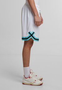 Weiße sportive Shorts mit einem elastischen Bund, türkisfarbenen und schwarzen Akzenten am Saum, kombiniert mit weißen/roten Turnschuhen und weißen Socken.